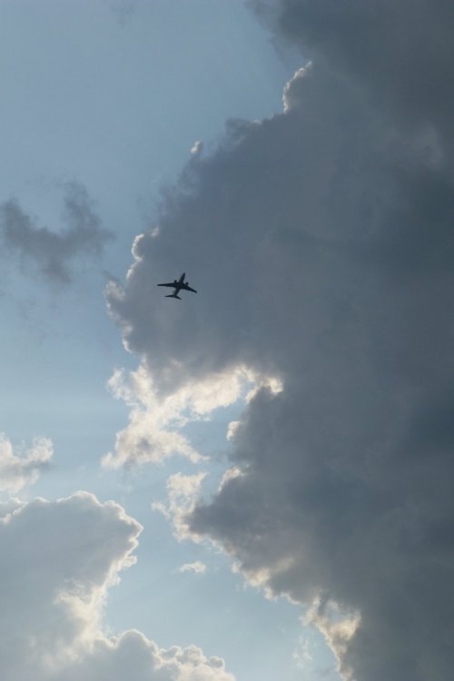 Un avion passe dans un ciel lumineux auquel les sombres nuages donnent du contraste. L'avion, c'est mon père ingénieur, parti pour son dernier vol, sans instruments, sans compas, sans carte...